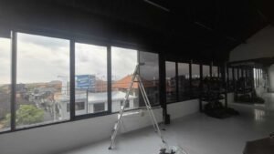 Proses pemasangan kaca film gedung di Bali dengan pemandangan atap bangunan khas Bali di latar belakang