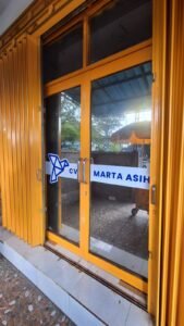 Pemasangan kaca film gelap pada pintu kaca toko di Bali dengan stiker branding CV Marta Asih.