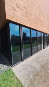 Pemasangan kaca film reflektif gelap pada dinding kaca full-height gedung di Bali