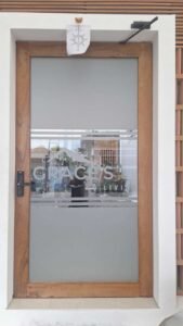 Sticker Sandblast custom logo Grace's Co Living pada kaca pintu kayu bingkai jati di Bali