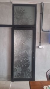 Sticker Sandblast motif daun palem dan monstera pada kaca pintu bingkai besi hitam di Bali