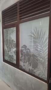 Sticker Sandblast motif daun monstera dan palem pada kaca jendela bingkai kayu rumah di Bali