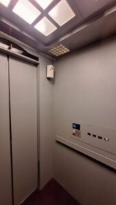 Sticker Solid warna abu-abu muda pada dinding samping interior lift dengan panel kontrol difabel di Bali