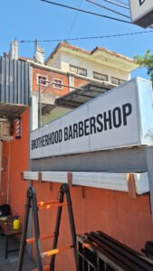 Cutting sticker huruf hitam Brotherhood Barbershop pada papan nama neon box
