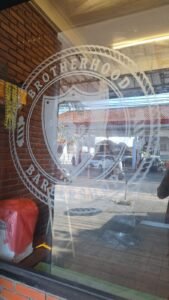 Cutting sticker sandblast logo Brotherhood Barbershop pada kaca etalase depan