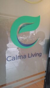 Cutting sticker logo Calma Living warna hijau dan biru pada pintu kaca sandblast