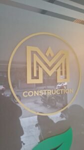 Cutting sticker emas logo M Construction pada kaca sandblast kantor