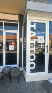 Cutting sticker putih jam buka dan QR code Instagram pada pintu kaca studio tattoo di Canggu