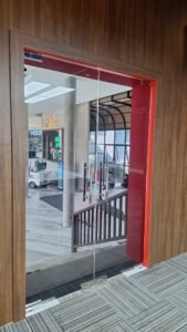 Kaca film bening pada pintu kaca frameless dengan kusen merah di area lobby Bali International Golf