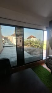 Kaca film gelap pada pintu kaca geser kamar dengan pemandangan atap rumah
