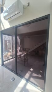 Kaca film gelap pada pintu kaca geser besar rumah dengan kusen aluminium hitam