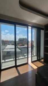 Kaca film pada pintu kaca geser kamar dengan pemandangan langit dan atap rumah