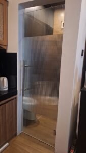 Sticker kaca motif ribbed fluted pada pintu kaca frameless kamar mandi